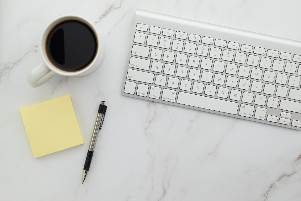Keyboard, coffee and a yellow sticky note on a marble desk