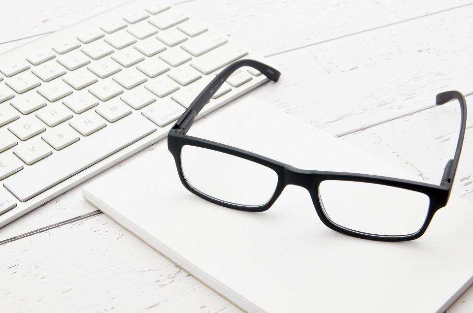 Glasses resting next to a white keyboard