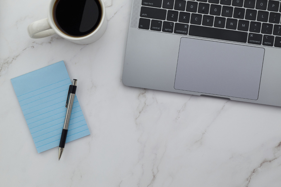 Blue notepad, pen and laptop on a marble desk